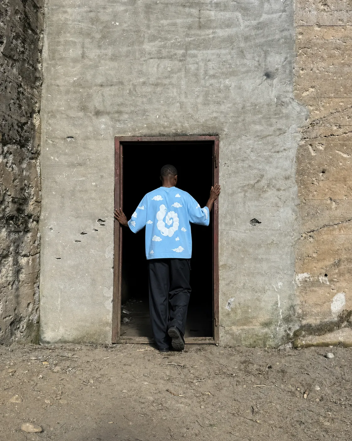 Cloud 9 T-shirt shown from the back in a weathered doorway